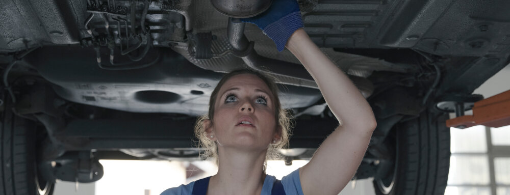 A female mechanic is checking the exhaust system of the car, (speedalternators.com).